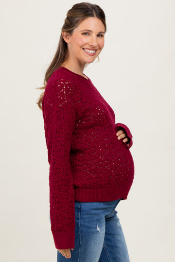 woman wearing a burgundy maternity sweater with lace detail and blue jeans, showing her baby bump