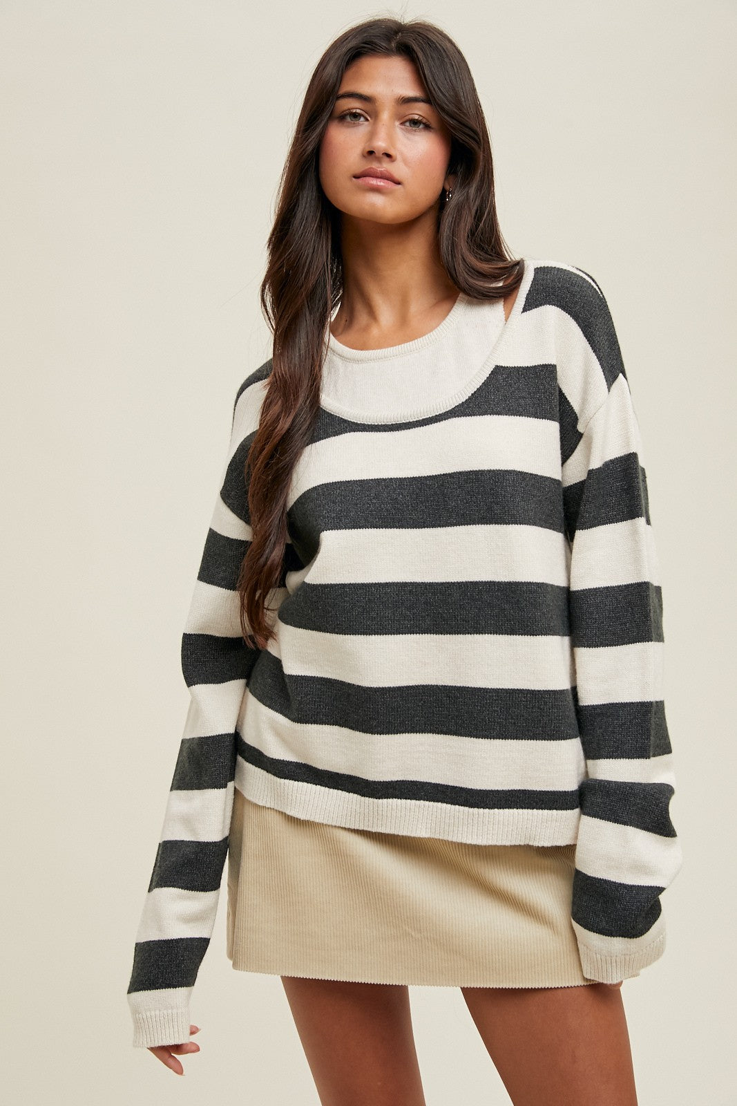 woman wearing a striped black and cream oversized sweater paired with a beige mini skirt