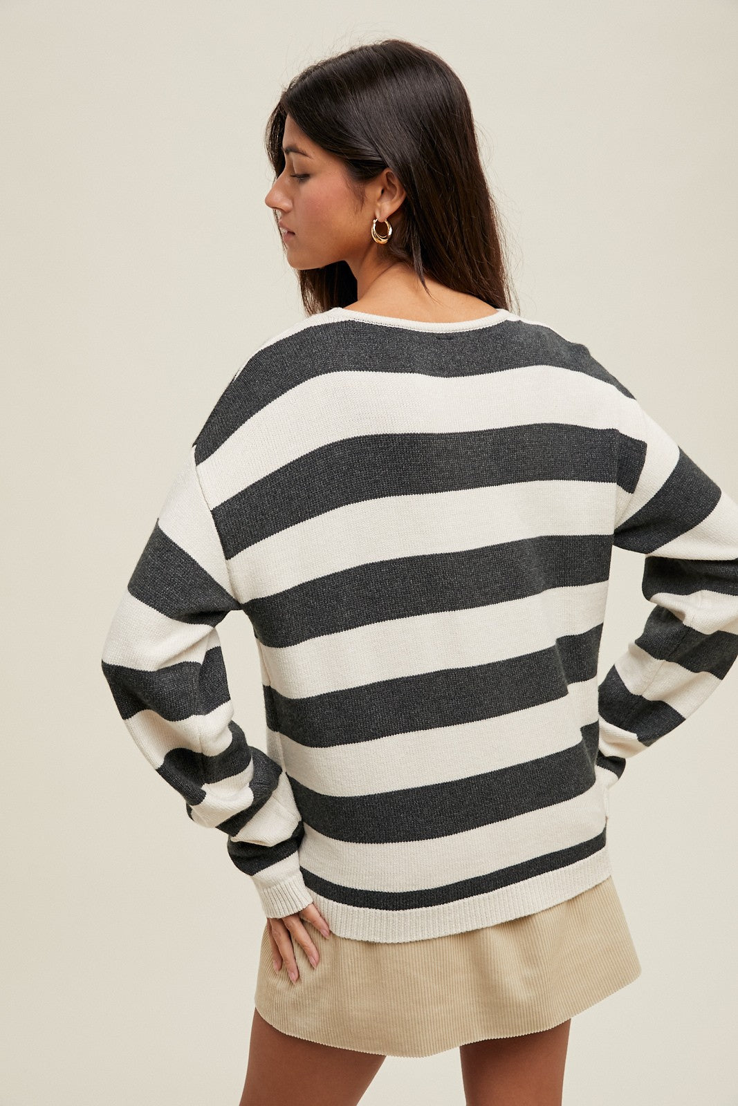 woman wearing a black and white striped oversized sweater with long sleeves, styled with a beige skirt