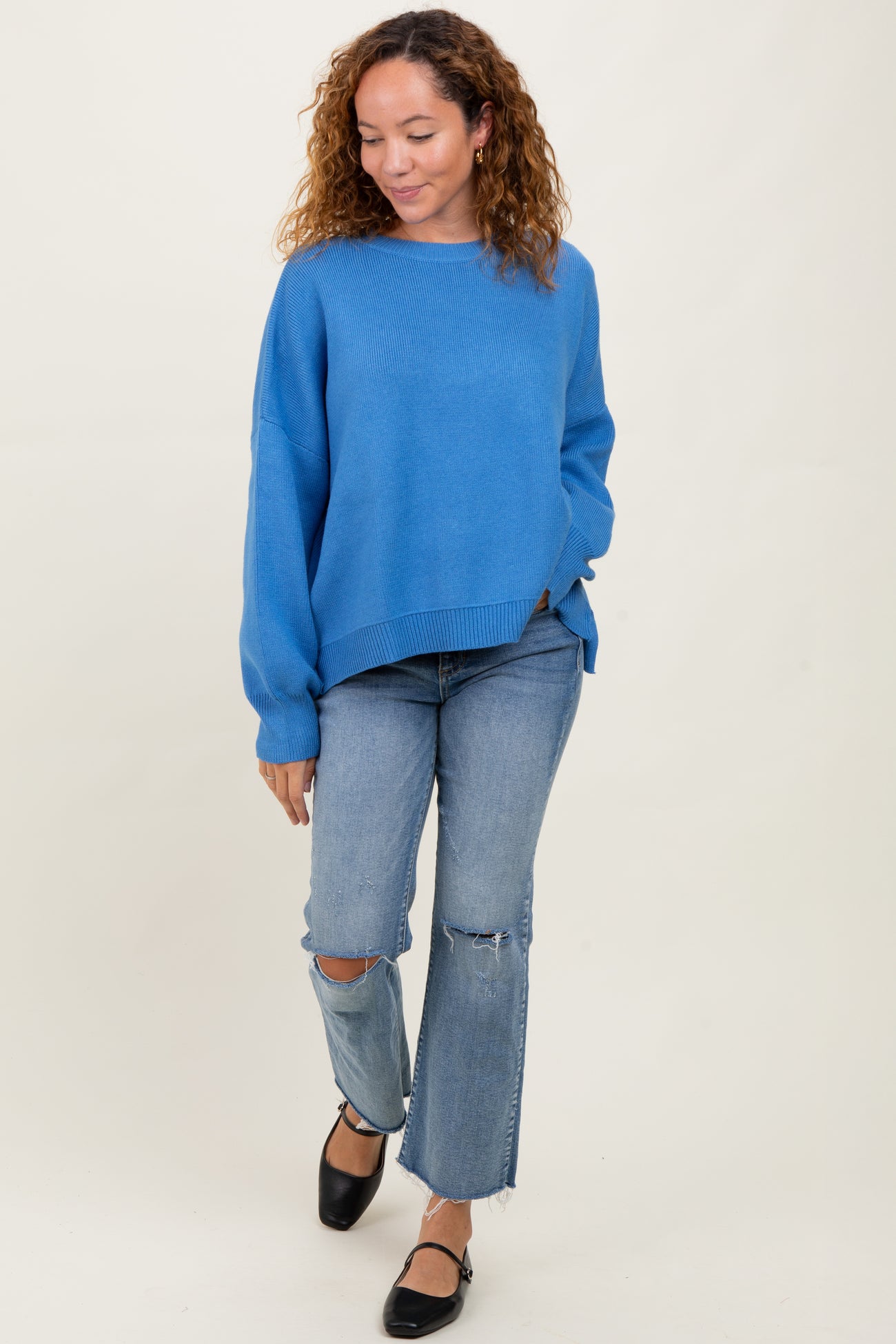 woman wearing a knitted blue oversized sweater with dropped shoulders and light wash distressed jeans