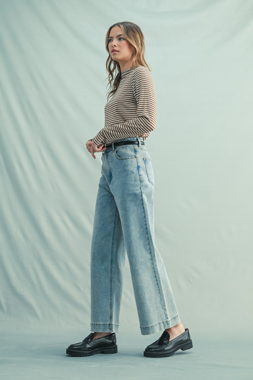 woman wearing a striped long sleeve top and light blue high-waisted wide-leg jeans with black loafers