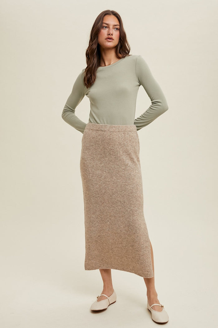 woman wearing a light green long sleeve top and a beige knitted midi skirt with a side slit