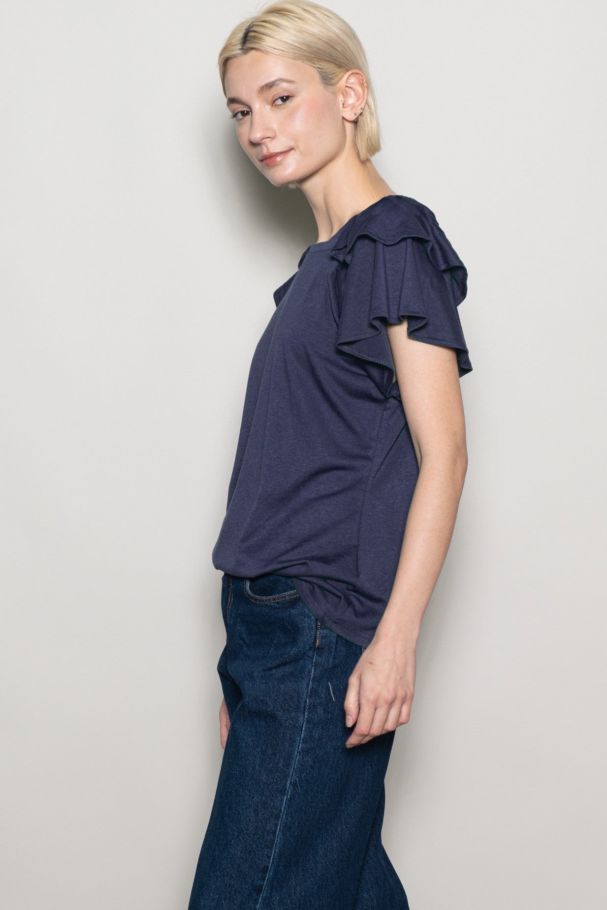 woman wearing a navy blue short sleeve top with ruffle details, paired with dark denim jeans