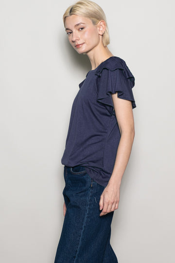 woman wearing a navy blue short sleeve top with ruffle details, paired with dark denim jeans
