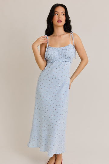 woman wearing a light blue sundress with floral print and adjustable tie straps, styled in a relaxed pose