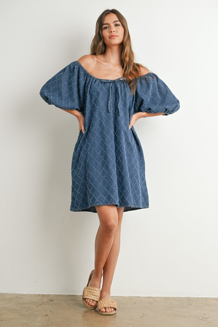 woman wearing a navy off-the-shoulder denim dress with puff sleeves and a relaxed fit, posing against a white background