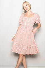 woman wearing a pink and white gingham puff sleeve dress with a smocked bodice and tiered skirt