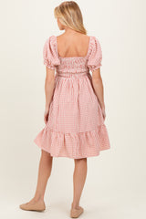woman wearing a coral and white gingham maternity dress with puff sleeves and ruffle hem, showing her back
