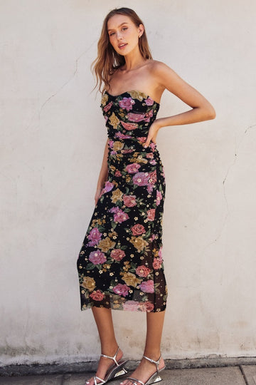 woman wearing a black floral mid-length dress with a sweetheart neckline and ruched detailing