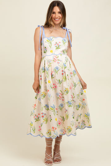 woman wearing a floral maternity dress with spaghetti straps and a scalloped hem, styled with strappy heels