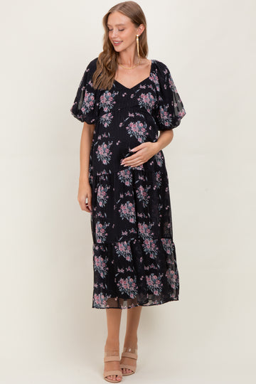 woman wearing a black floral print maternity maxi dress with puff sleeves and a visible baby bump