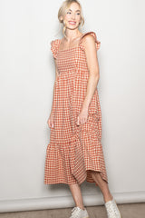 woman wearing a rust and cream gingham maxi dress with ruffle straps and tiered skirt, styled with white sneakers