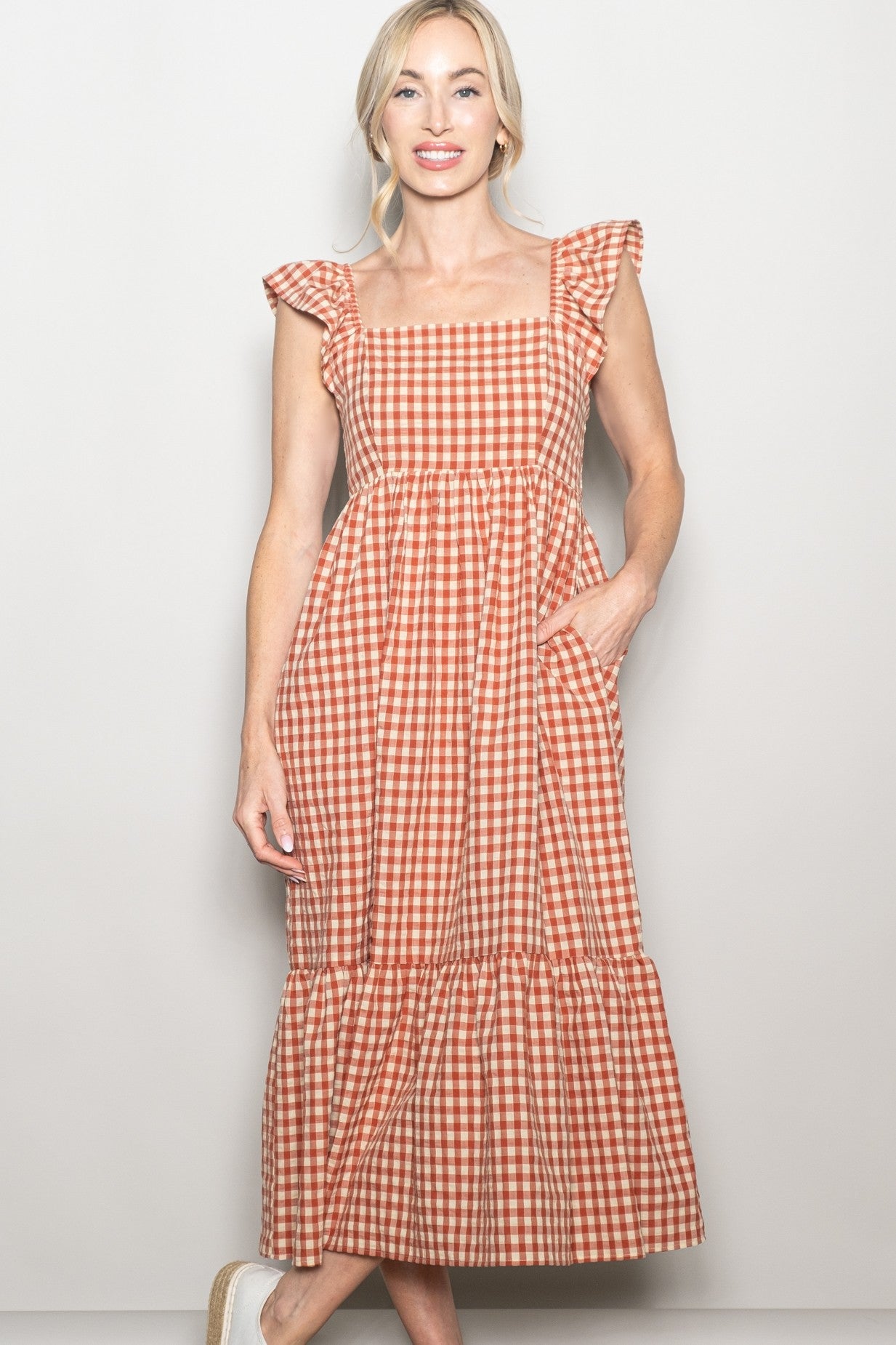 woman wearing a rust and cream checkered maxi dress with ruffled sleeves and pockets
