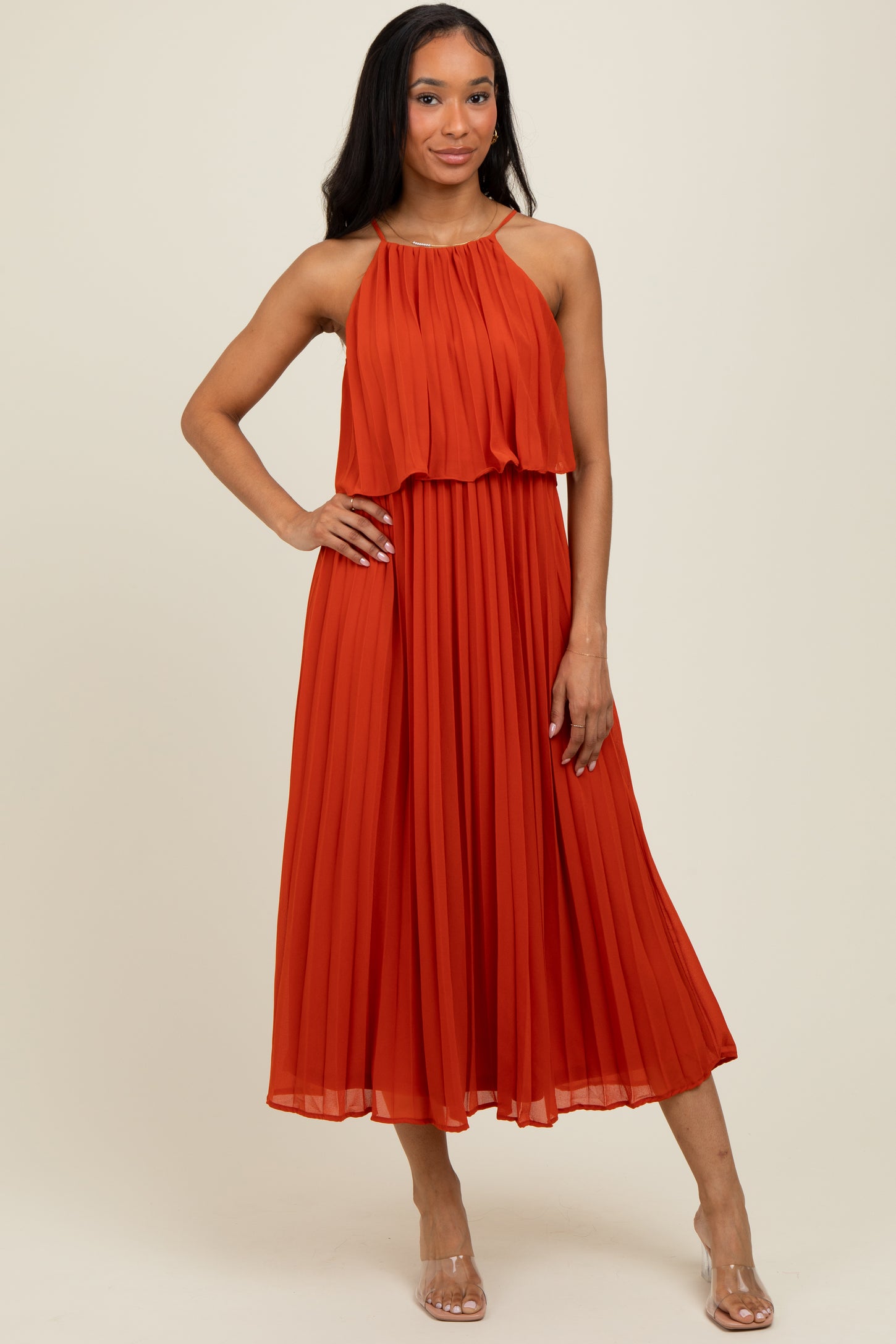 woman wearing an orange pleated midi dress with a halter neckline and layered bodice