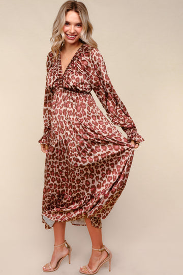 woman wearing a brown leopard print maternity dress with a v-neck and long sleeves, holding the hem while smiling