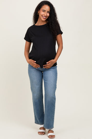 woman wearing a black ribbed maternity top and blue jeans, gently cradling her baby bump