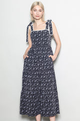 woman wearing a navy blue floral print midi dress with tie shoulder straps and side pockets