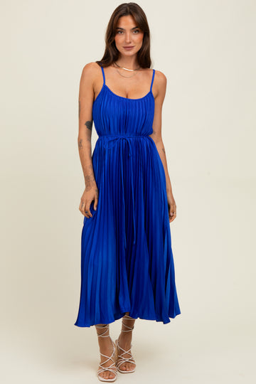 woman wearing a bright blue pleated midi dress with spaghetti straps and a tie waist detail.