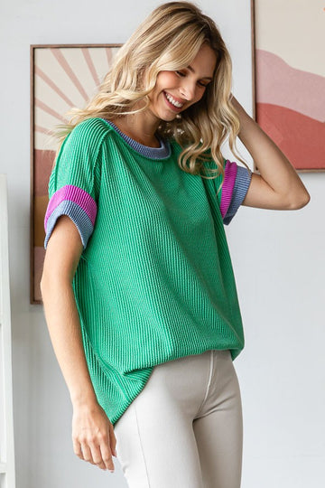woman wearing a green ribbed short sleeve top with colorful striped cuffs and a relaxed fit