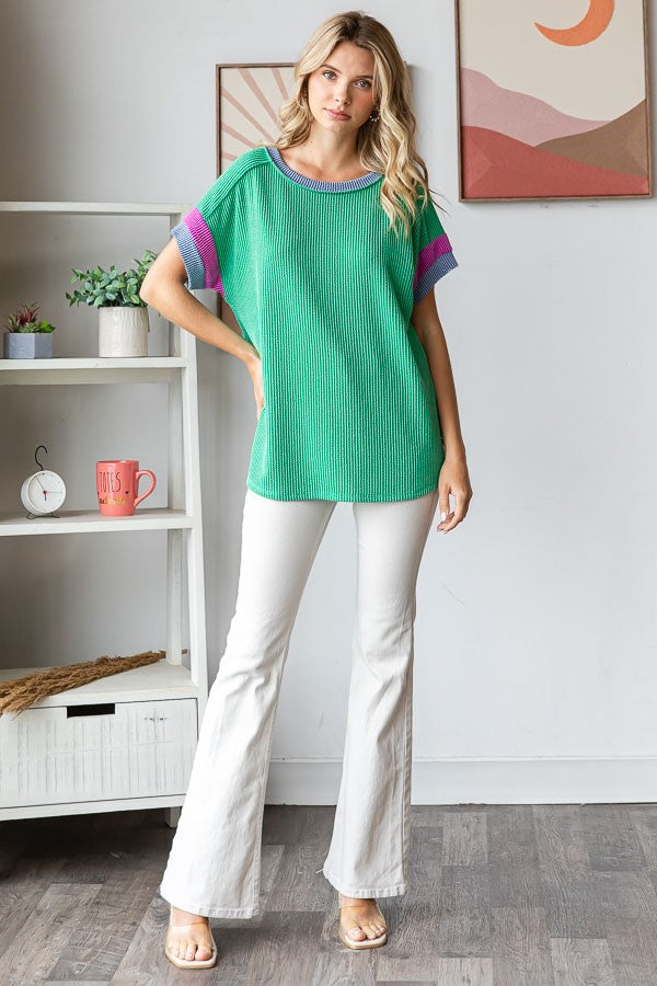 woman wearing a green striped oversized top with purple accents and white flared jeans