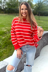 woman wearing a red and white striped oversized sweater and distressed light blue jeans, smiling outdoors