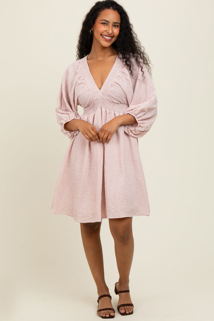 woman wearing a pink and white striped short dress with a deep v-neck and puff sleeves
