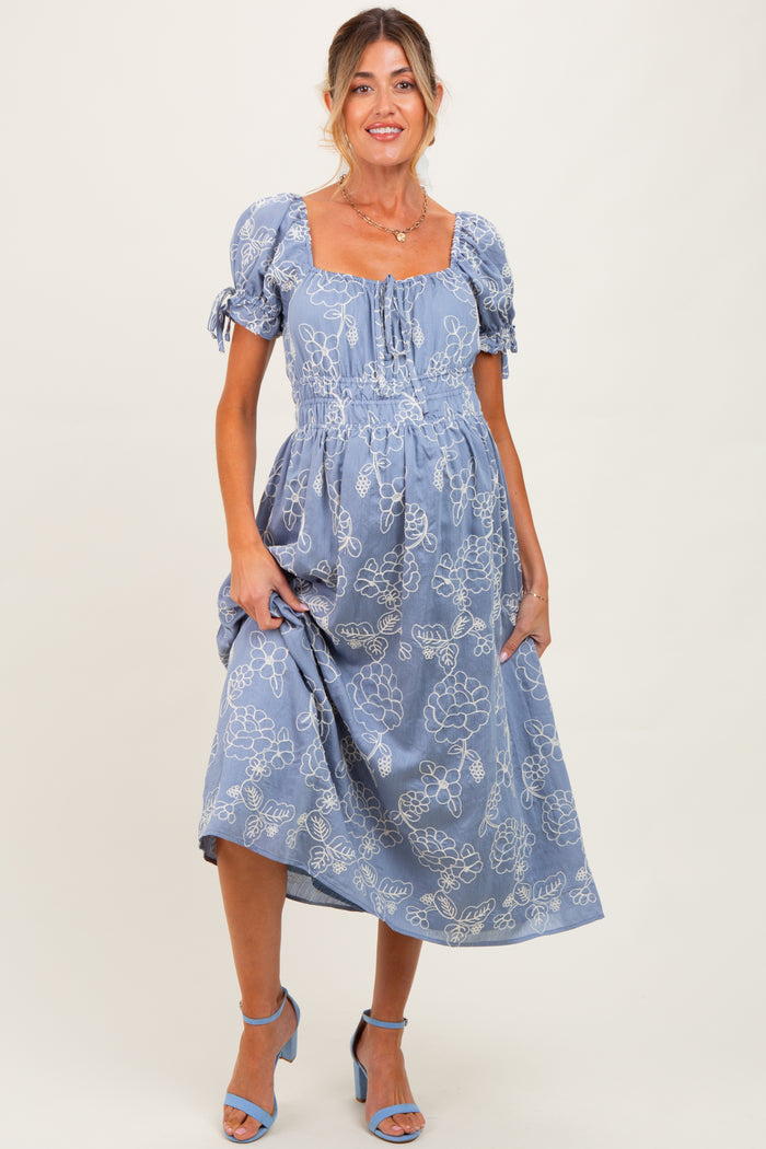 woman wearing a blue floral maternity dress with puff sleeves and a baby bump visible.