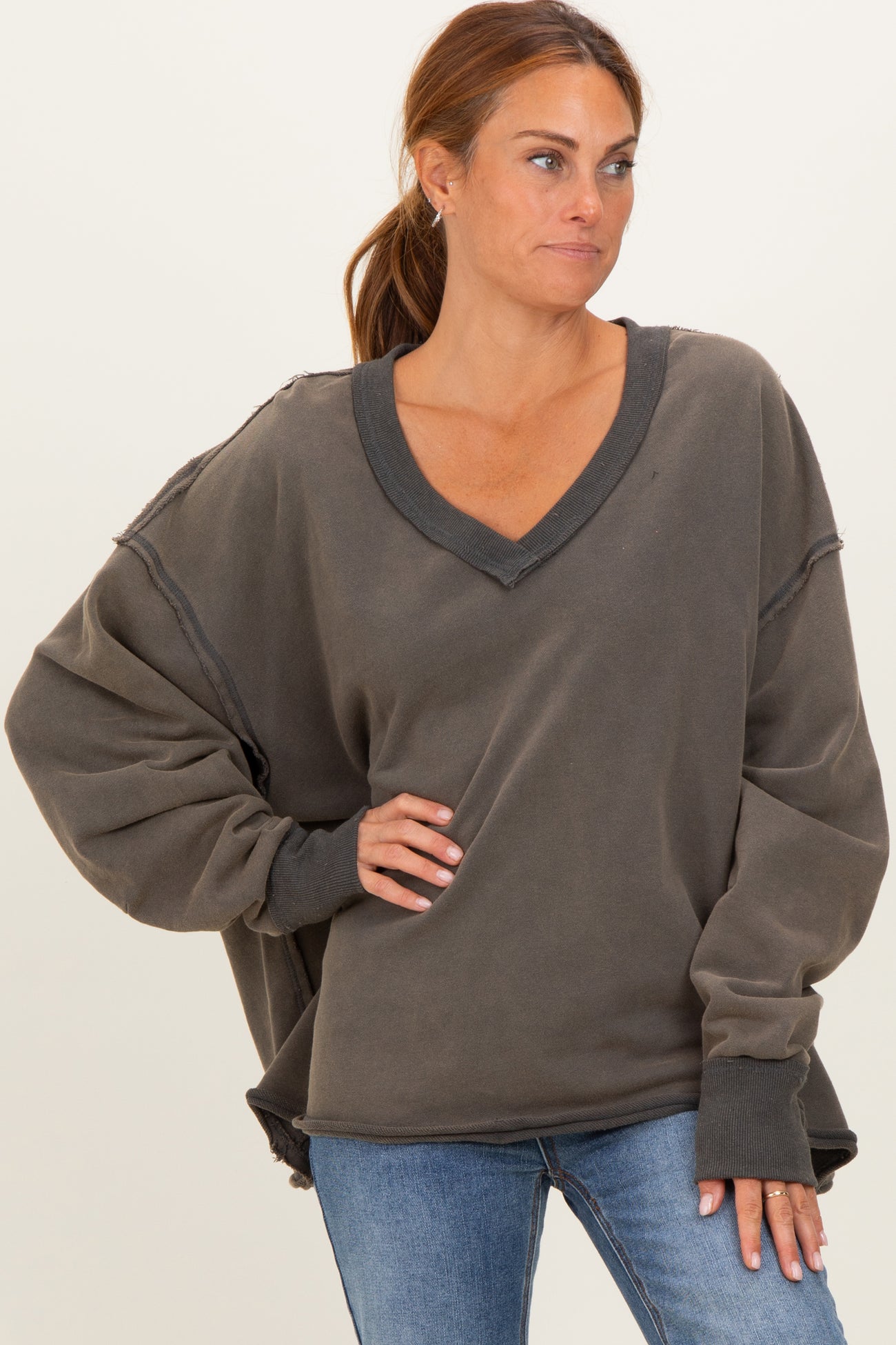 woman wearing a charcoal oversized v-neck sweatshirt with loose sleeves and distressed details, paired with blue jeans