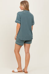 woman wearing a teal short sleeve loungewear set with matching shorts and white trim, viewed from the back