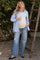 woman wearing a light blue striped maternity shirt and a beige tank top, with a visible baby bump, paired with distressed wide-leg jeans