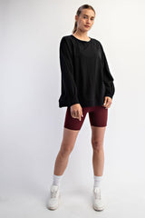 woman wearing a black oversized sweatshirt and burgundy bike shorts, standing with hands in pockets