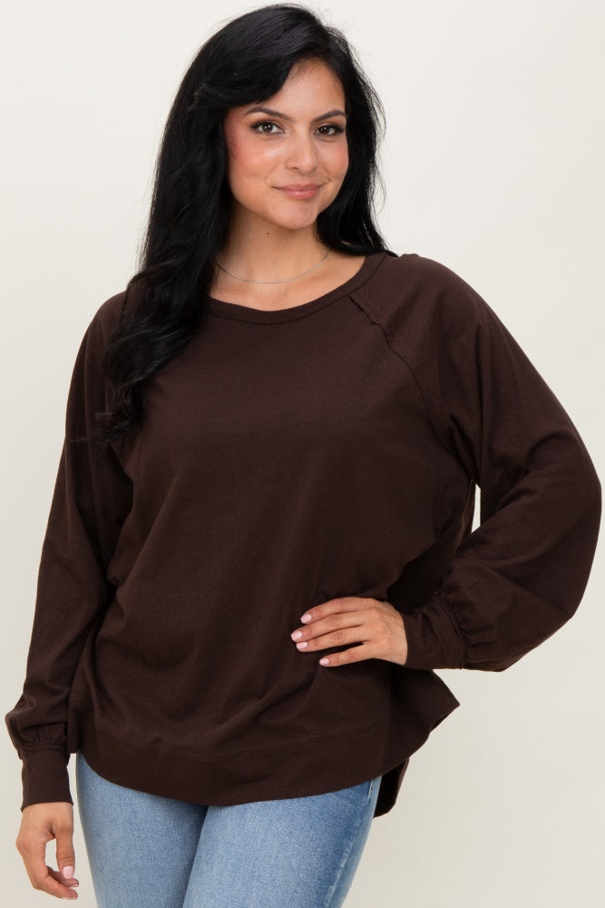 woman wearing a brown long sleeve top with a relaxed fit and raglan sleeves, paired with light blue jeans