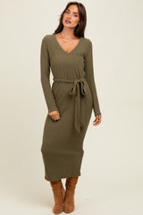 woman wearing an olive green ribbed midi dress with a v-neck and tie waist, standing and looking off to the side