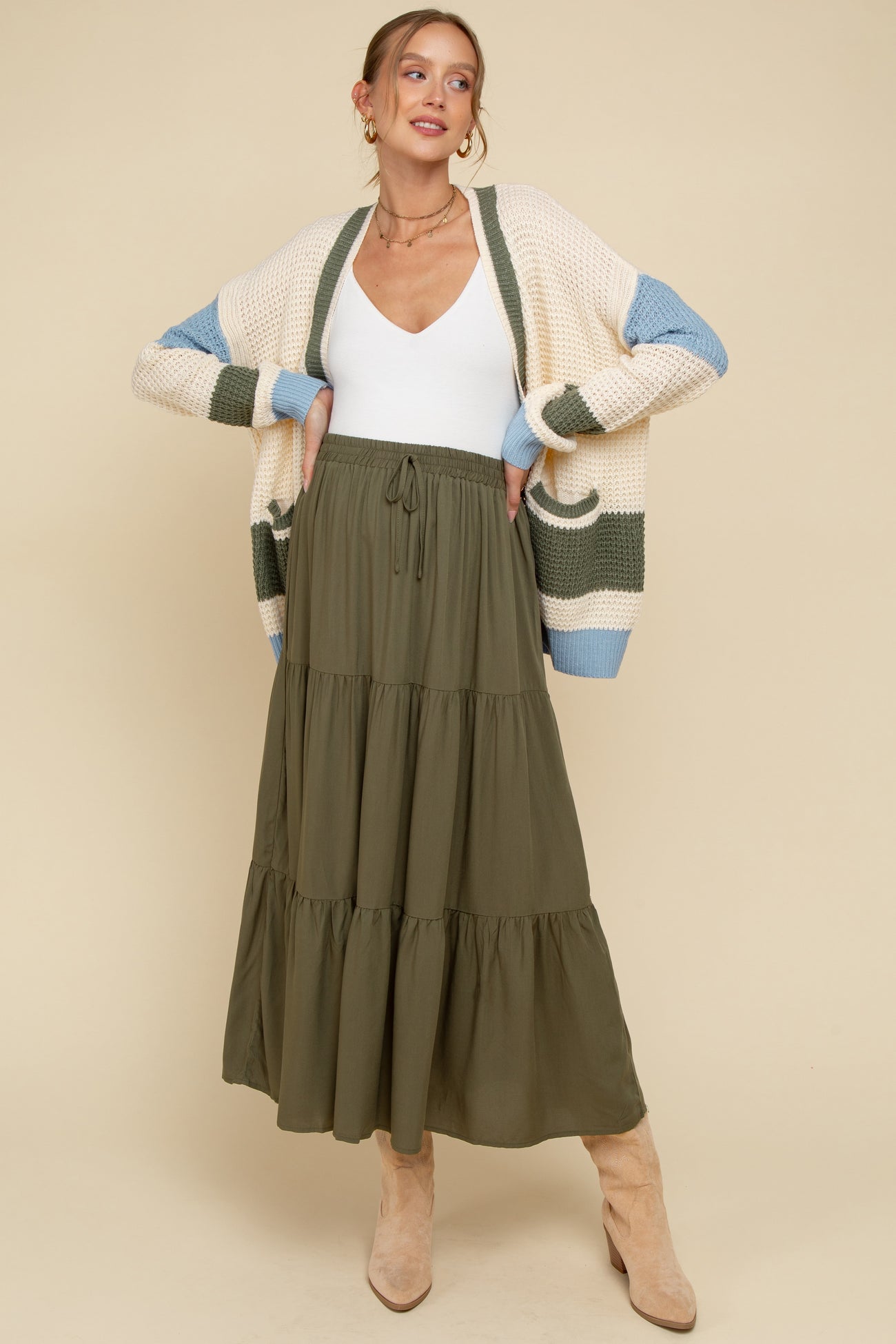 woman wearing a white maternity top and an olive green tiered maxi skirt, styled with a beige and blue cardigan