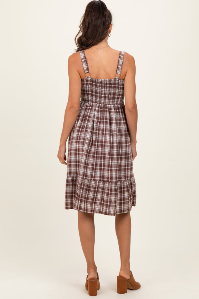 woman wearing a brown plaid smock dress with adjustable straps and a tiered skirt, viewed from the back