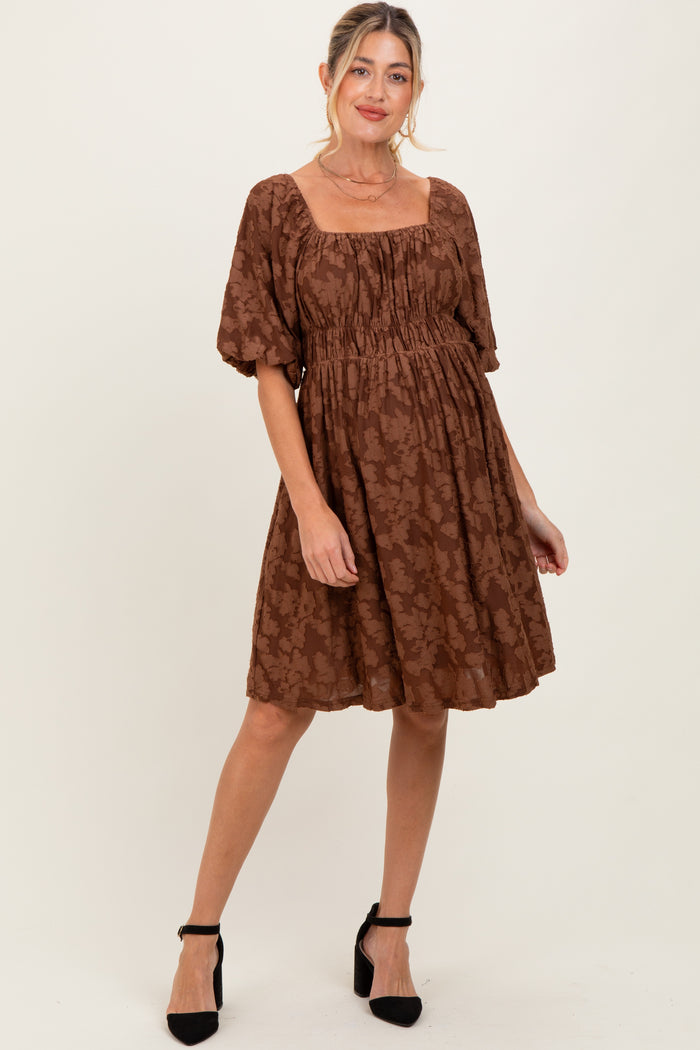 woman wearing a brown floral maternity dress with puff sleeves and a square neckline, standing and smiling