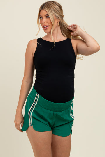 woman wearing a black maternity tank top and green athletic shorts with white side stripes, showing her baby bump