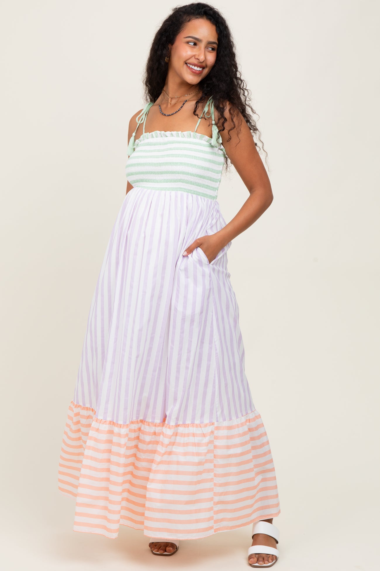 woman wearing a mint green and lavender striped maternity maxi dress with side pockets and a tiered orange striped hem