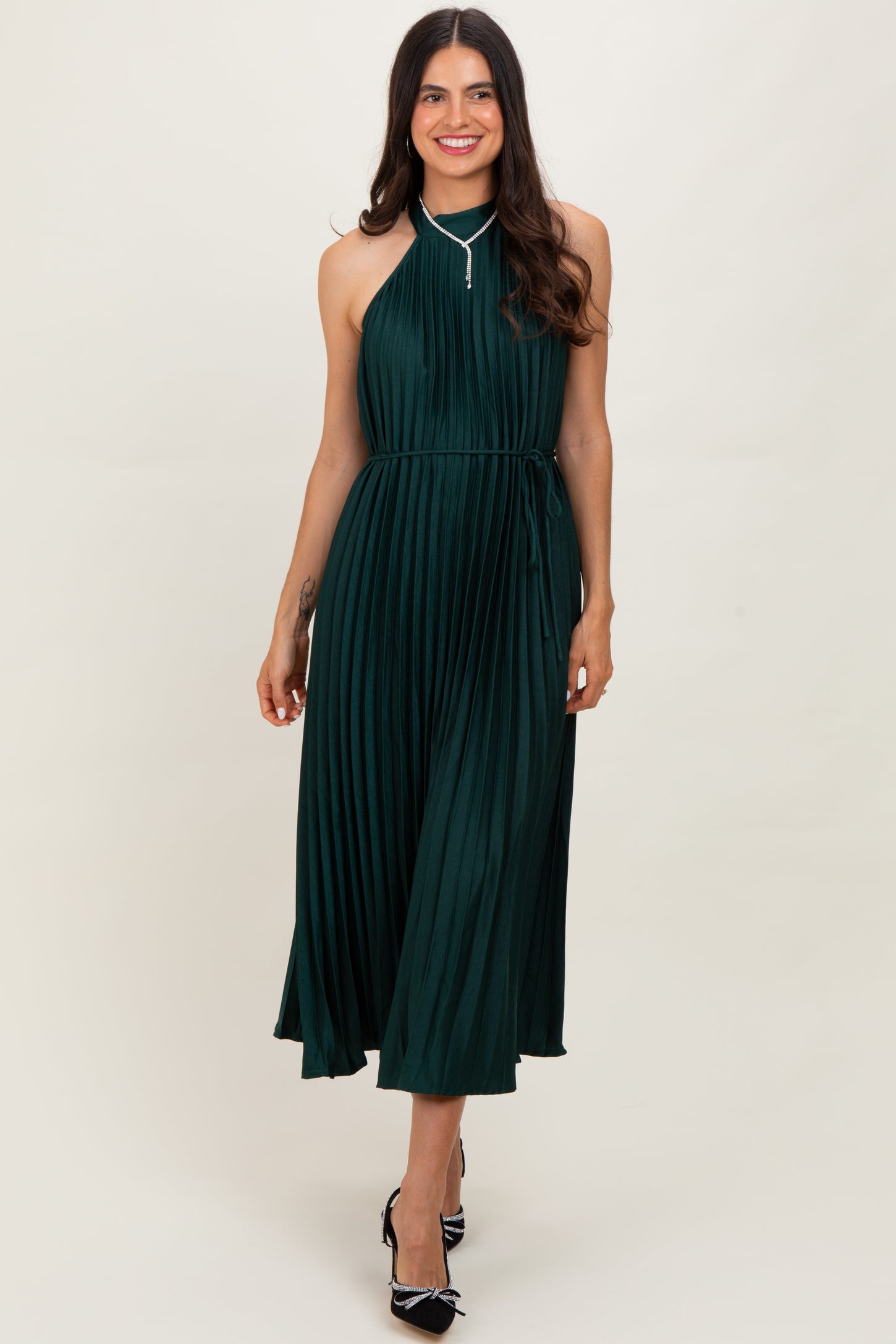 woman wearing a dark green pleated halter neck dress with a tie waist and a flowing skirt