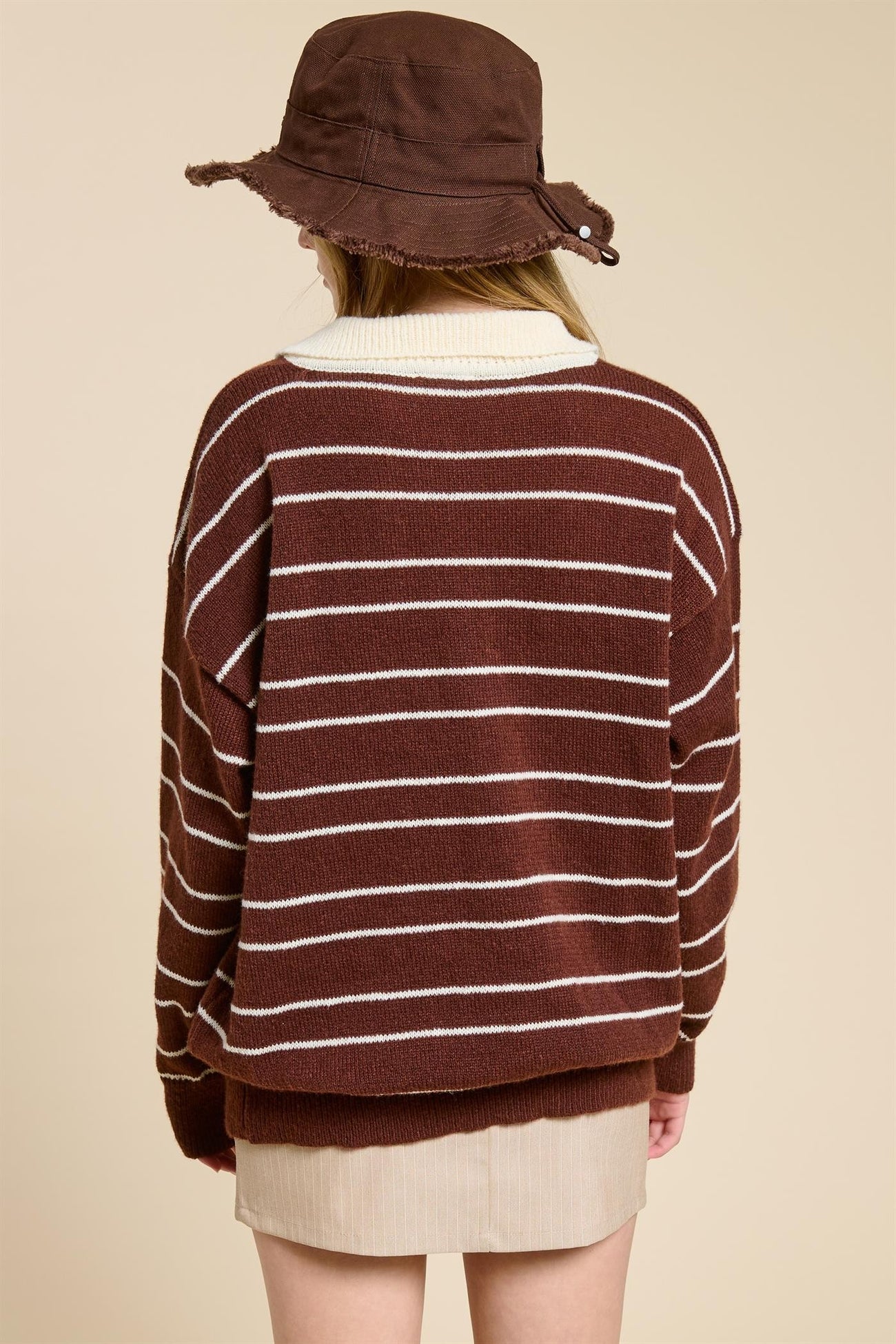woman wearing a brown and white striped oversized sweater with a wide neckline and a brown bucket hat