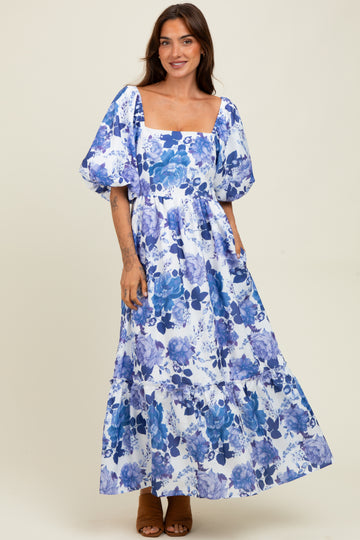 woman wearing a white maxi dress with blue floral print and puff sleeves, standing on a beige background