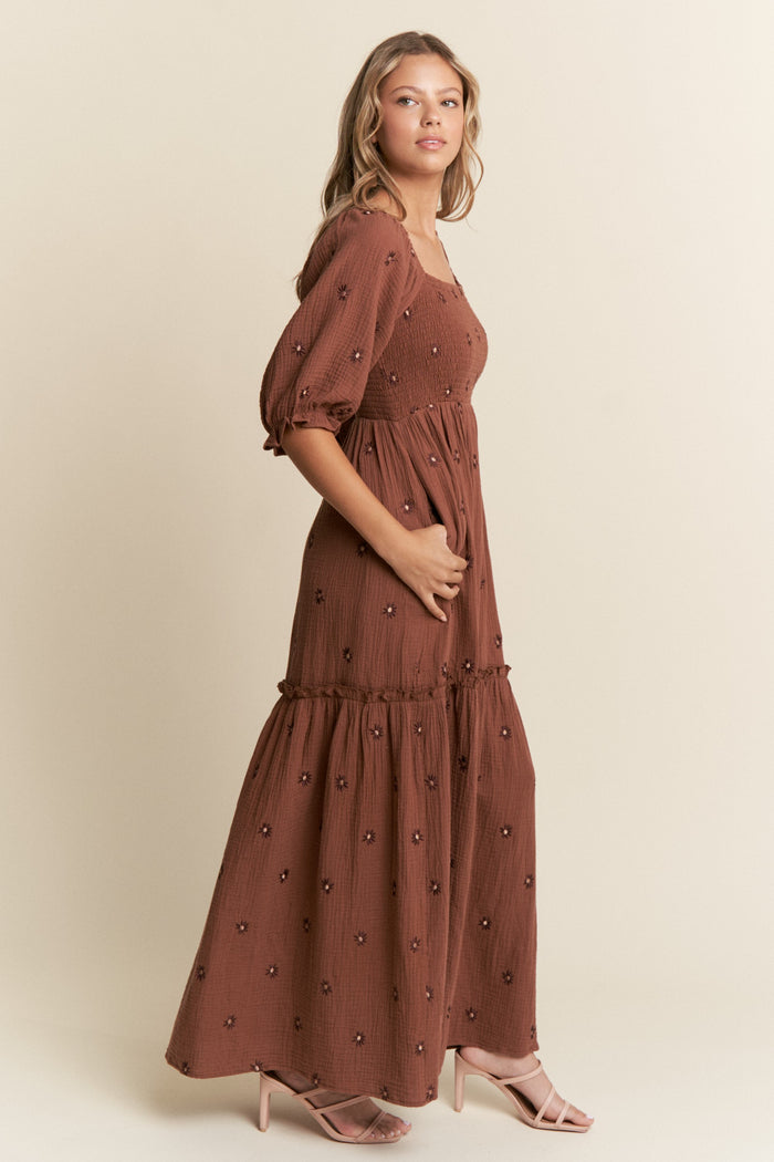 woman wearing a rust-colored maxi dress with puff sleeves and floral embroidery