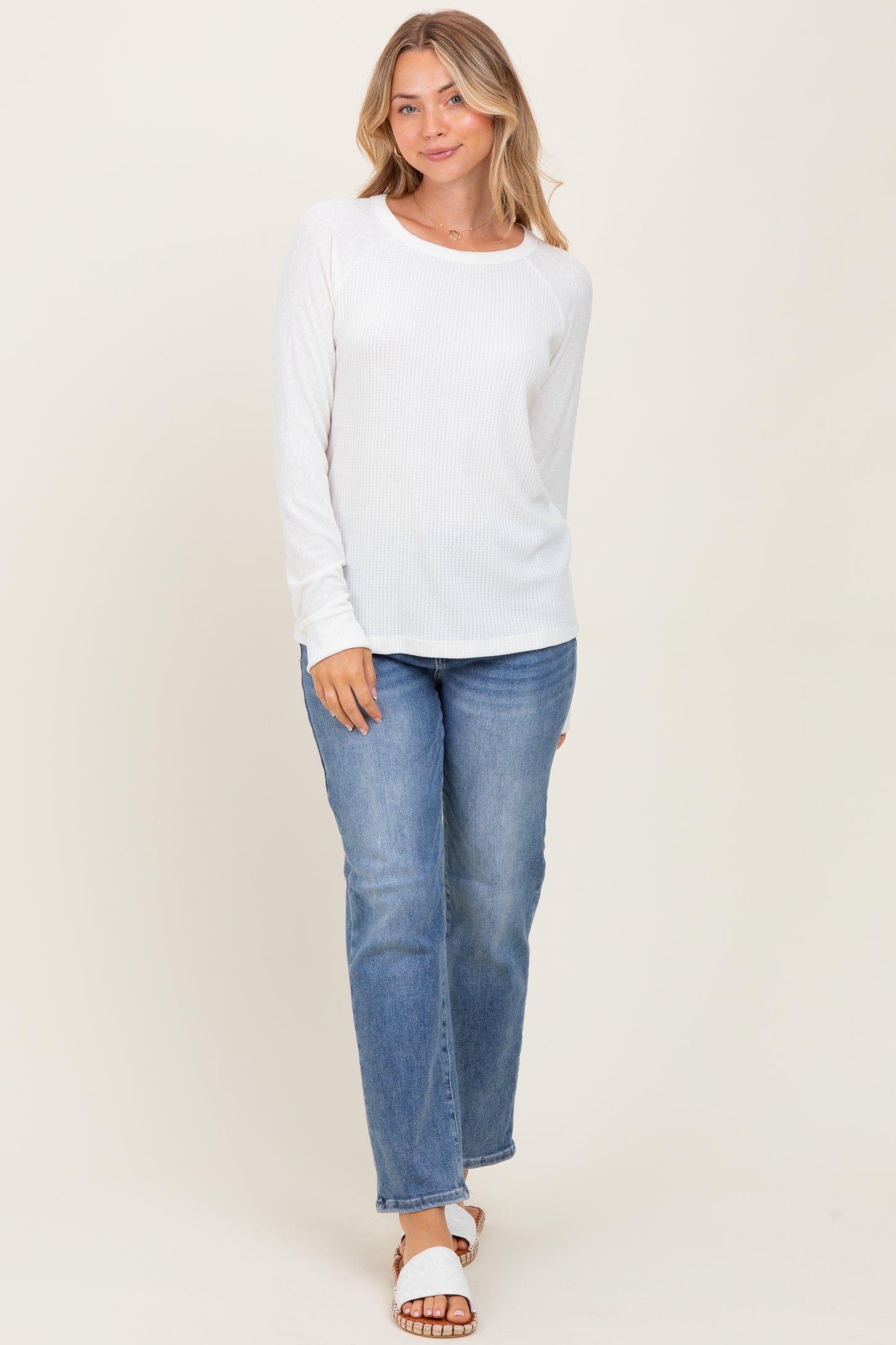 woman wearing a white long sleeve ribbed top with a round neckline and blue straight leg jeans