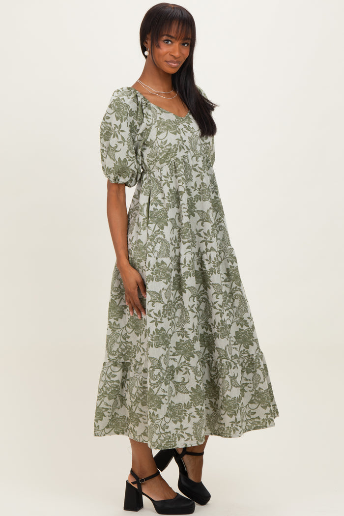 woman wearing a green floral print midi dress with puff sleeves and a tiered skirt, standing against a plain background