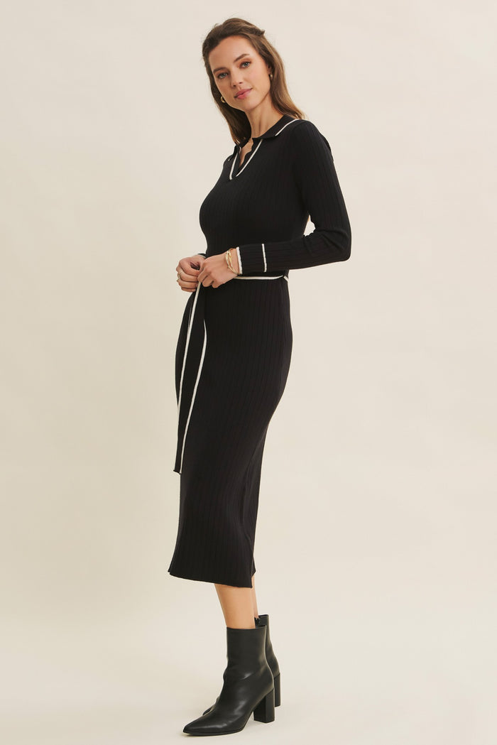 woman wearing a black ribbed knit midi dress with a v-neck and white trim, styled with ankle boots
