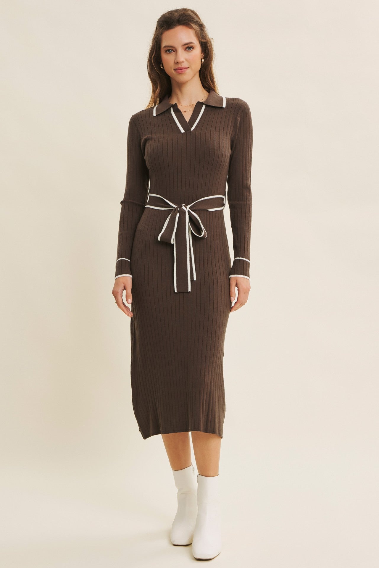 woman wearing a brown ribbed midi dress with a collar and white trim, cinched at the waist with a matching belt