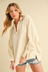 woman wearing a light beige oversized pullover sweatshirt with button detailing and rolled sleeves, paired with distressed denim shorts