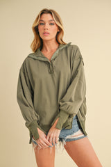 woman wearing an olive green oversized pullover sweatshirt with a half-zip and rolled sleeves, paired with denim shorts