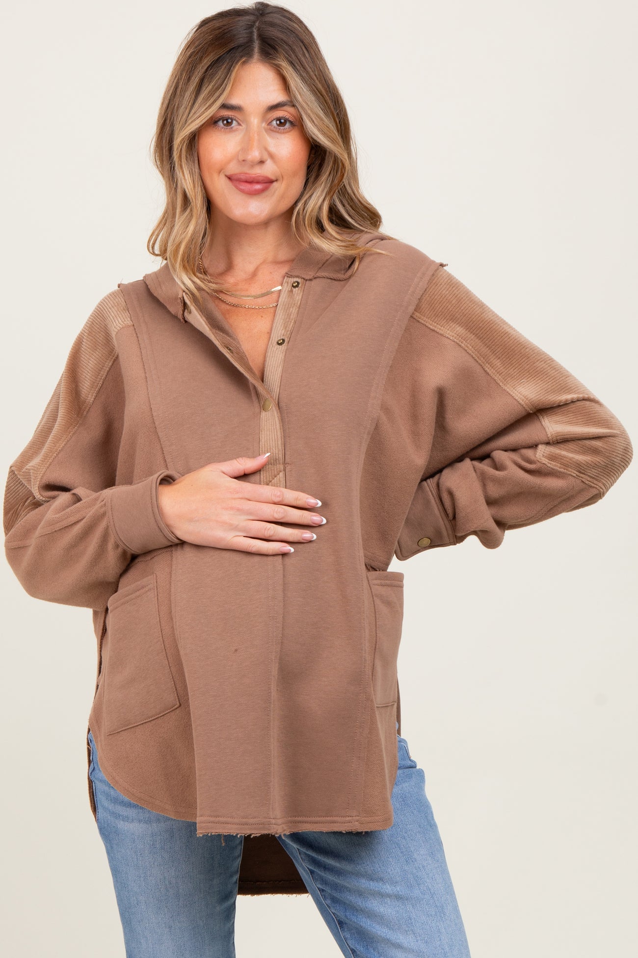 woman wearing a brown maternity hoodie with buttons and pockets, holding her baby bump