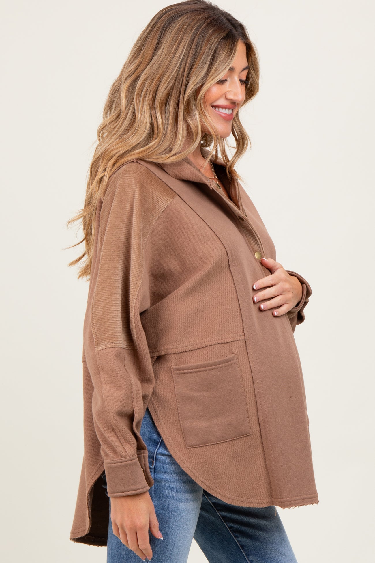 woman wearing a brown maternity pullover with a collar and pockets, gently cradling her baby bump